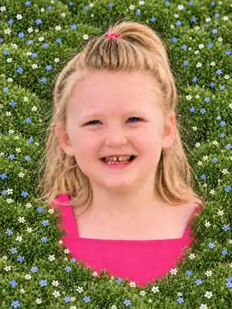 Lila smiling in a pink dress, surrounded by Irish moss with tiny white and blue flowers covering both sleeves.
