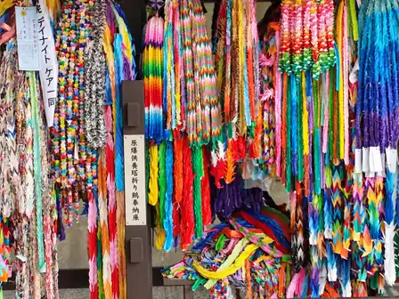 Colorful handmade paper crane offerings hanging in dense strands around a Japanese memorial sign