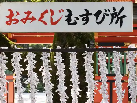 White paper fortunes tied beneath a Japanese sign, with a mossy tree and vermilion shrine behind