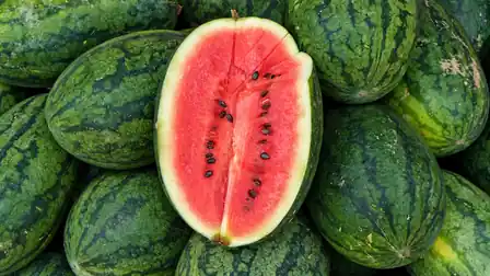 A cut red watermelon among whole green watermelons