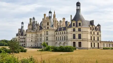 Château de Chambord with its many slate turrets, stone chimneys and long limestone facade beyond a dry lawn.