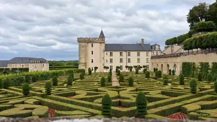 Château de Villandry and its keep beyond ornamental hedge patterns and tiered topiary, with terraces and trees at right.