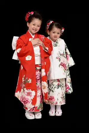Two children in red and cream floral kimono, standing together against deep black.